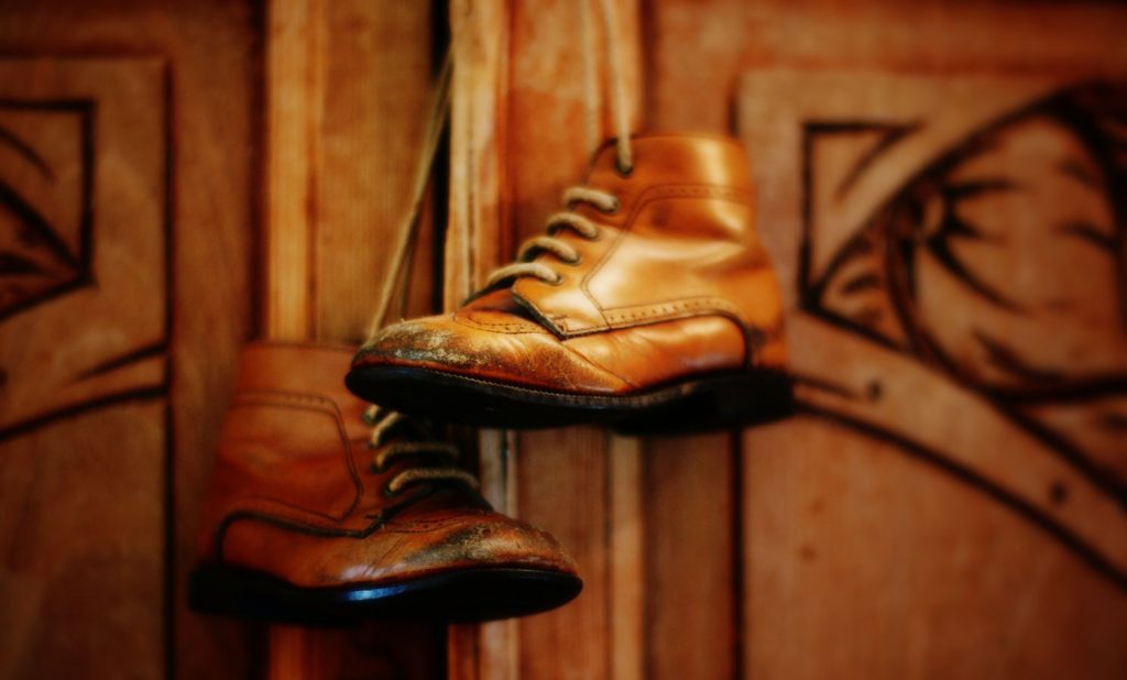 Une paire de veille chaussures d'enfant en cuir, usées au bout suspendue devant un buffet en bois de la même couleur.