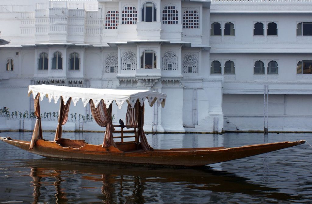 Un pigeon est posé sur un bateau en bois avec un baldaquin blanc. En arrière plan le palace flottant d'Udaipur au Rajasthan, Inde.