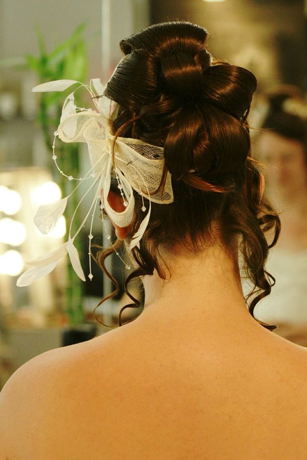 Chloé se fait faire son chignon de mariage dans un salon de coiffure à Saint Etienne. Il est décoré avec un ruban et des plumes blanches.