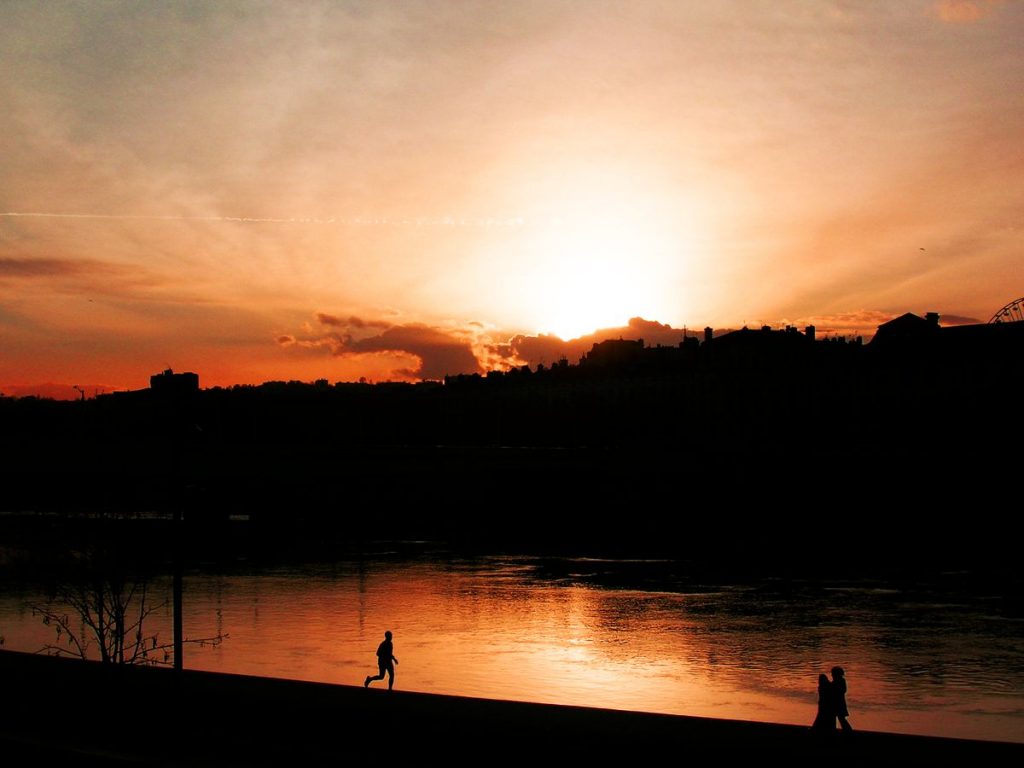 Le couché de soleil se reflète dans le Rhône à Lyon et une silhouette semble courir sur le fleuve. Un jeune couple s'enlace au bord de l'eau.