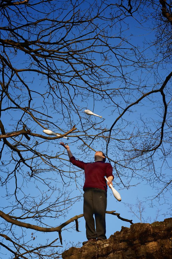 Martin fait de la jonglerie à trois massues au milieu des branches, en haut d'un monticule, au fort de Montessuy, à Caluire-et-Cuire.