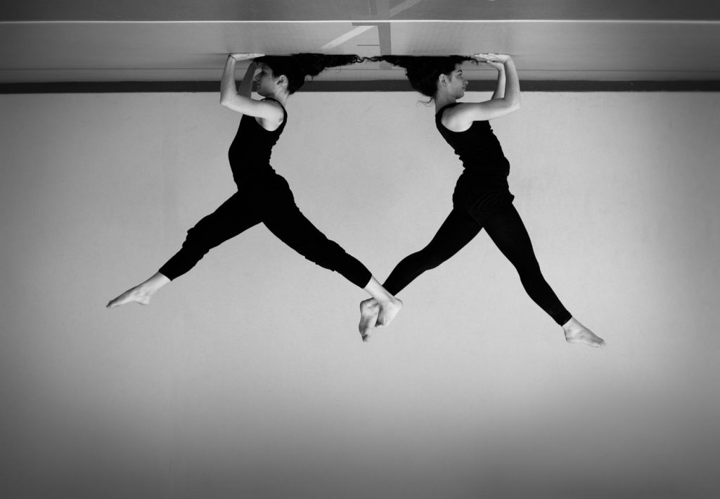 Julie et Mathilde, en trépied à Overground Circus, se retiennent par la jambe. Cette photo d'acrobatie, en noir et blanc, est présentée la tête en bas.
