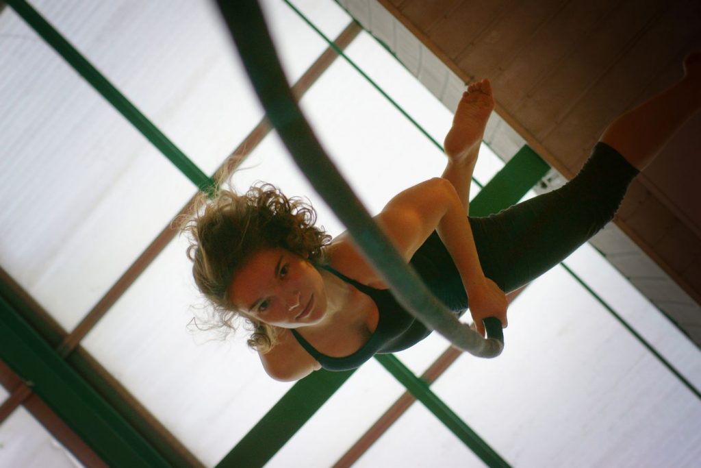 Margot fait de la corde lisse, La photo est prise d'en dessous. Au dessus d'elle, on voit la verrière du gymnase d'Overground Circus.