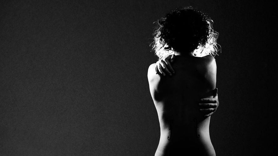 Photo en noir et blanc de Charlotte nue de dos avec ses mains posées sur une épaule et sur les côtes. Mais est-ce bien ses mains ?