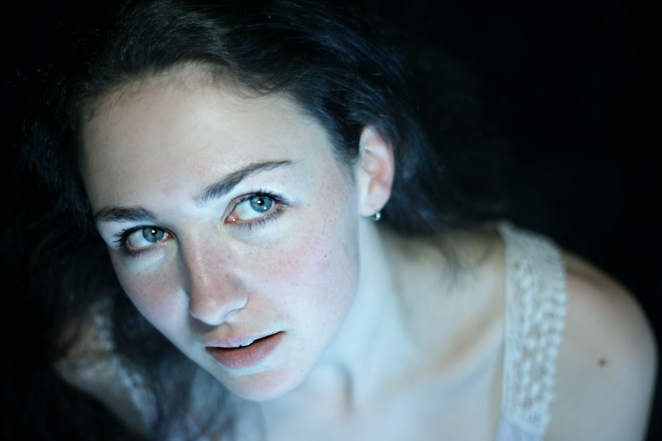 Portrait d'Iris qui porte un débardeur blanc avec de la guipure sur son épaule. Ses grands yeux bleus regardent sur le côté et elle ébauche un sourire.