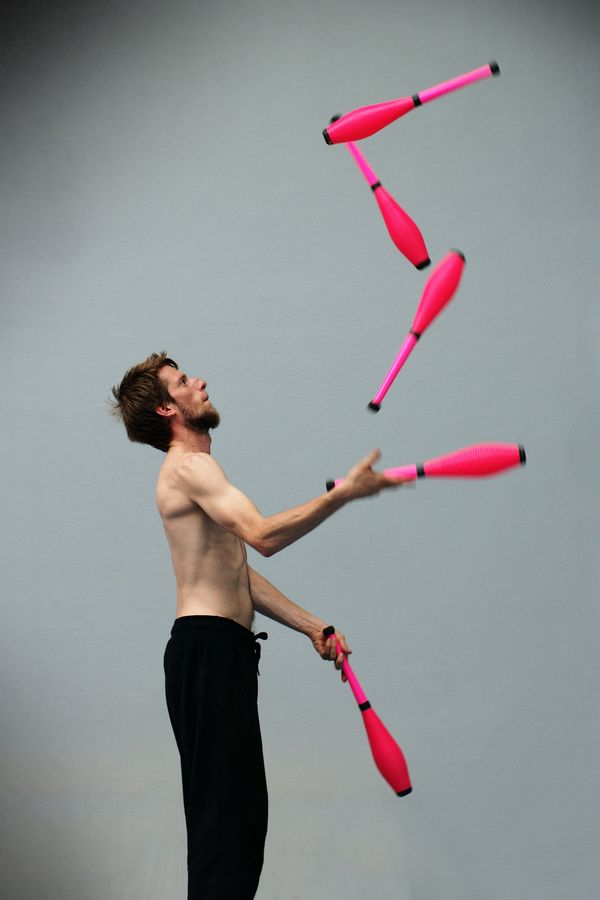 Maxime fait de la jonglerie avec 5 massues en simple tour au gymnase d'Overground circus à Lyon. Il est torse nu et jongle avec des massues roses.