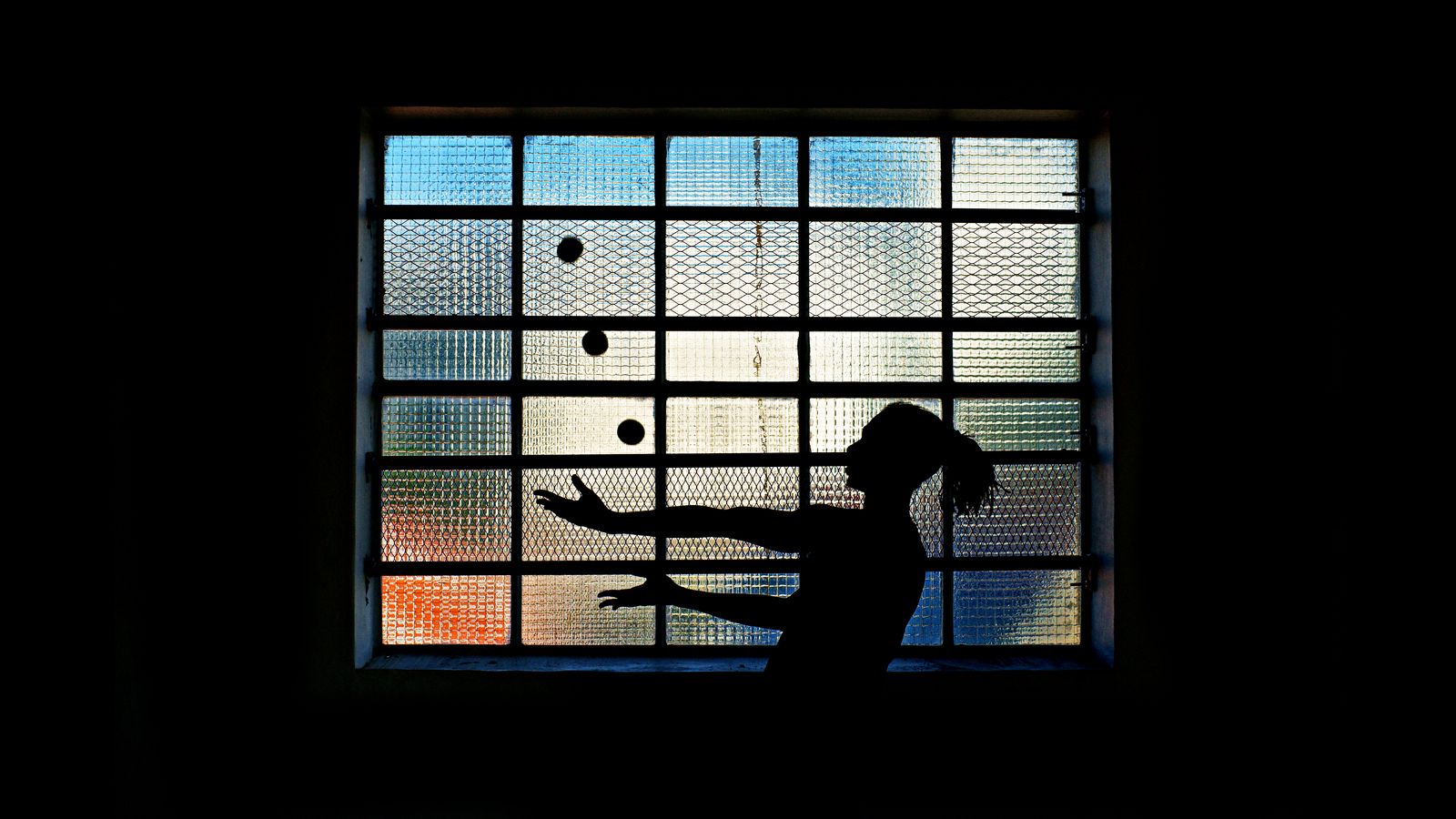 Jean-Souleyman, un jongleur lyonnais, jongle à trois balles devant une fenêtre à carreaux. La photo est prise en contre-jour et chaque balle a son carreau.
