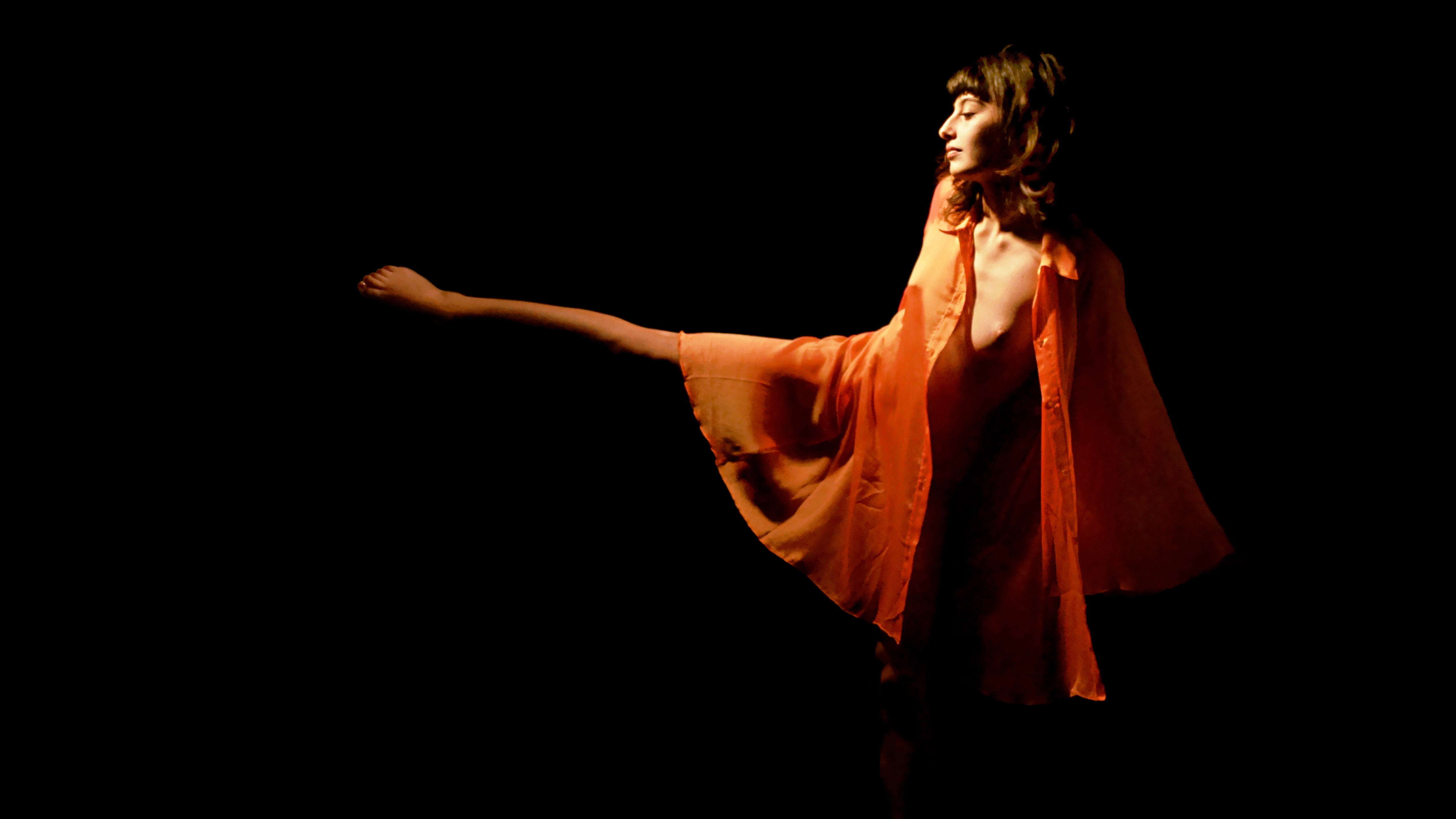 Maeva, nue sous une tunique orange transparente, danse. Sa jambe tendue sur le côté fait penser à une aiguille d'horloge enveloppée dans une cape orange.