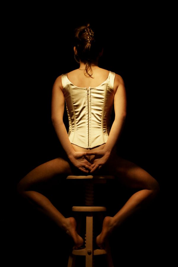 Maeva, en corset, dans la peau d'une danseuse est assise de dos sur un tabouret. Elle va bientôt finir de s'habiller en attendant le début du spectacle.