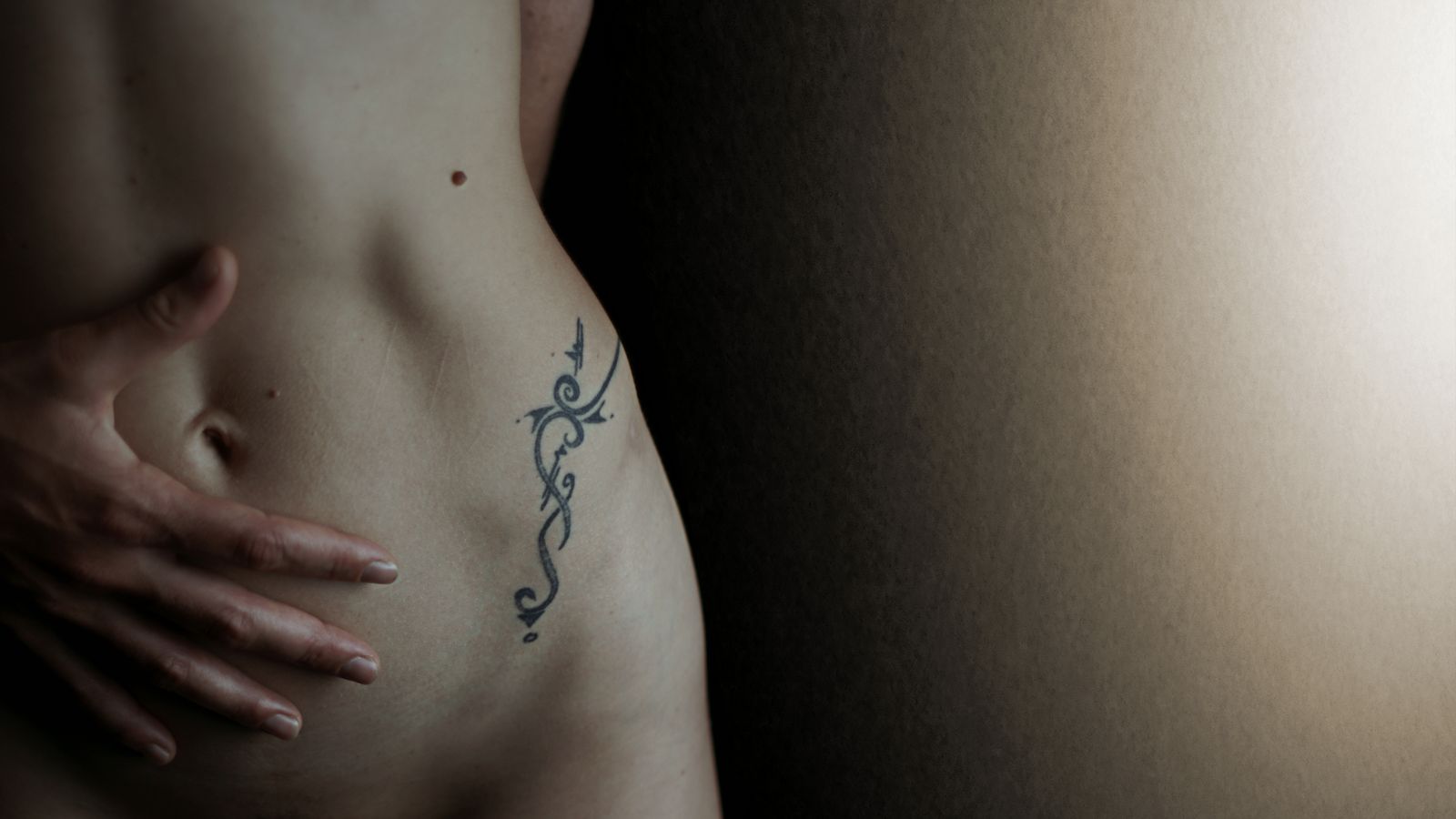 Céline a un tatouage tribal sur la hanche, juste à côté de petites coupures sur la peau de son ventre. Ses doigts sont posés autour de son nombril.