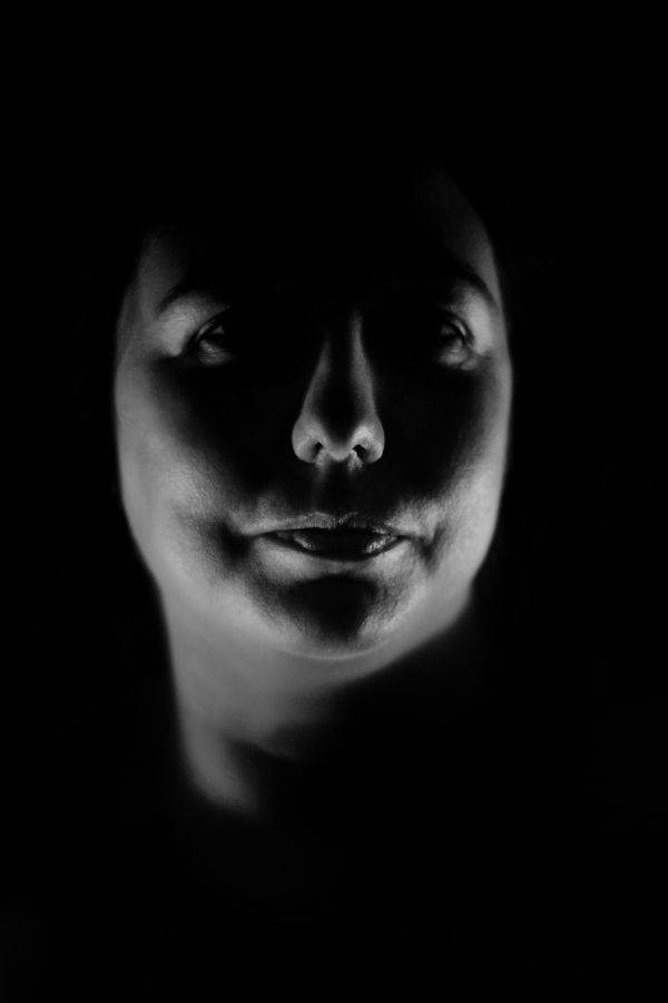 Portrait, en noir et blanc, très serré d'Anabelle en studio, chez moi, à Caluire-et-Cuire. Sa tête émerge de l'obscurité et n'est dessiné que par les ombres qui marquent les contours de son visage.