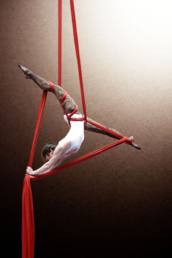 Claire Batissat fait un grand-écart dans un triangle formé par son tissu aérien. Pour cette séance au gymnase d'Overground Circus, l'acrobate portait un body blanc et des bas résilles.