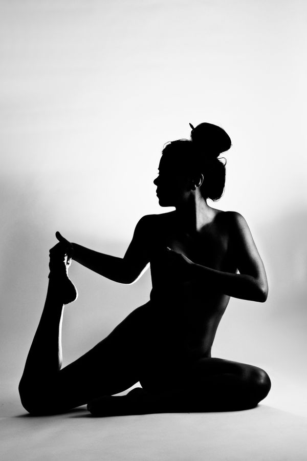 Ana, nue en studio fait des étirements de danse ou de cirque en contre-jour sur un fond blanc. On pourrait croire qu'elle en pleine séance de yoga.